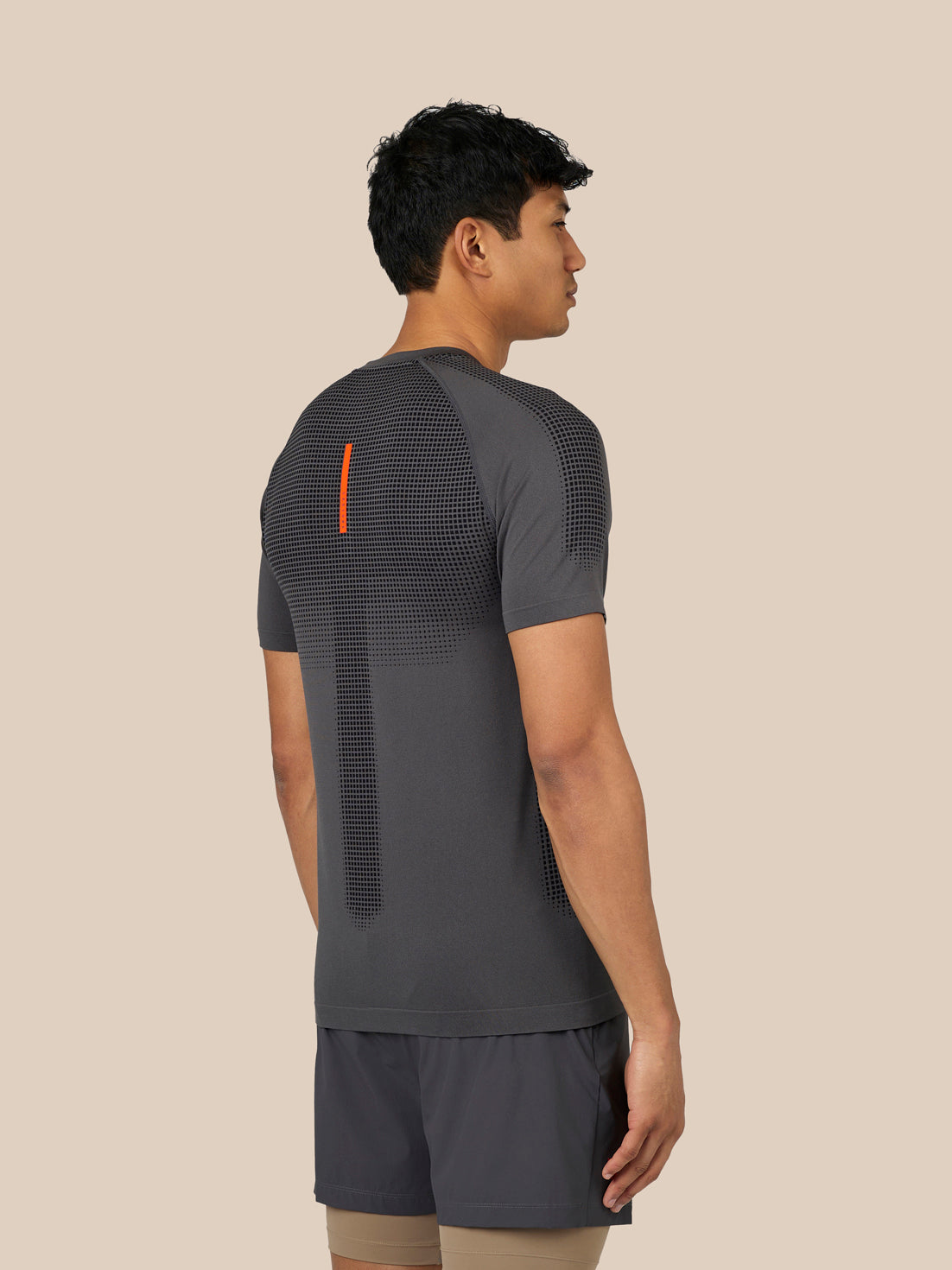 Back view of male model in dark grey Flow Training T Shirt with dotted back pattern and orange stripe detail