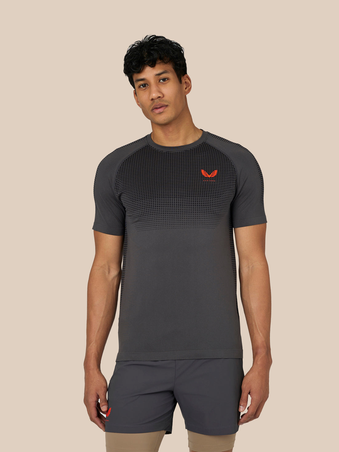 Male model wearing Flow Training T-Shirt in dark grey with dotted mesh pattern and red Castore logo on the chest.