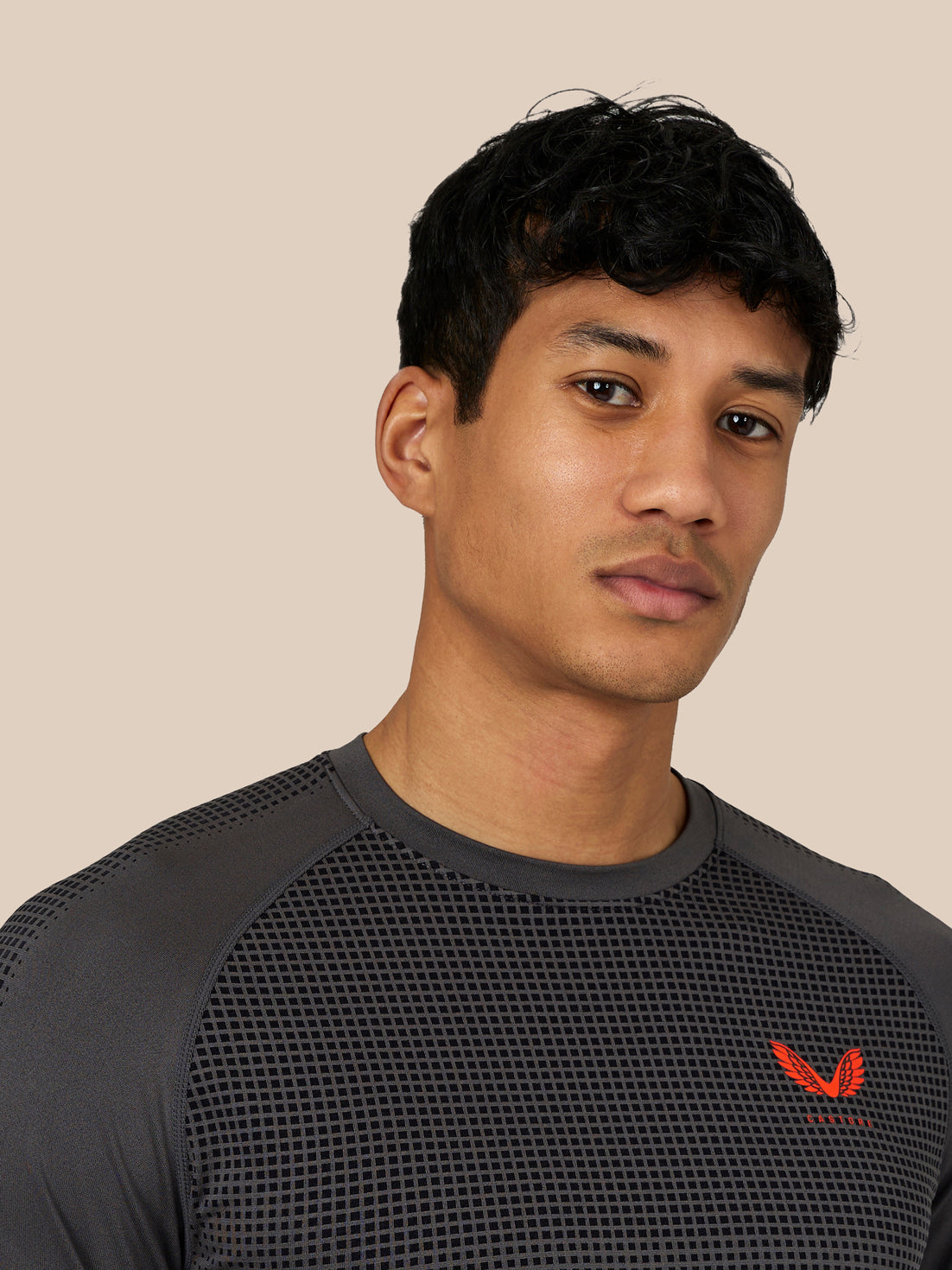 Close up of a male model wearing Flow Training T-Shirt in dark grey with a red Castore logo on the chest.