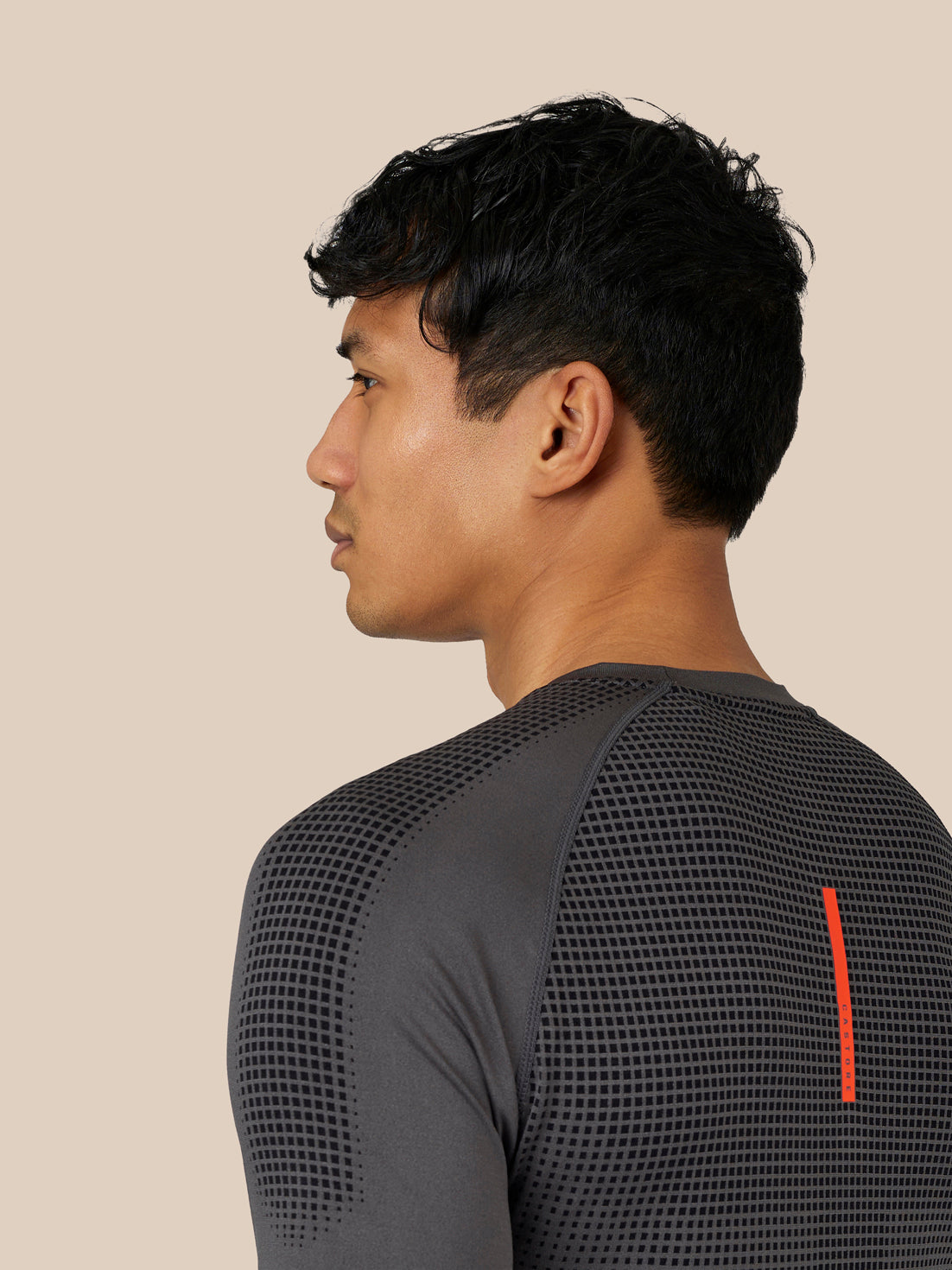 Side view of a male model wearing Flow Training T-Shirt in dark grey with dotted pattern on the back and a red vertical branding stripe.