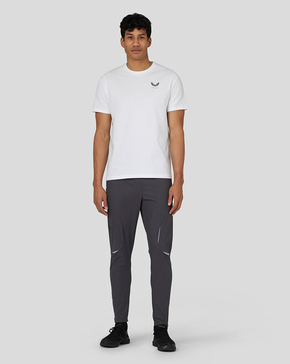 Full-body view of a man in a white Castore T shirt with dark athletic pants and black sneakers