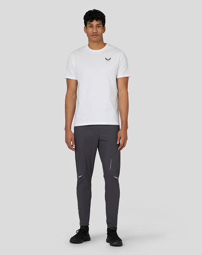 Full-body view of a man in a white Castore T shirt with dark athletic pants and black sneakers