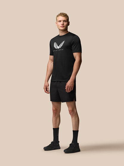 Full body view of a man in black Adapt Short Sleeve Graphic T Shirt with wings logo, paired with black shorts.