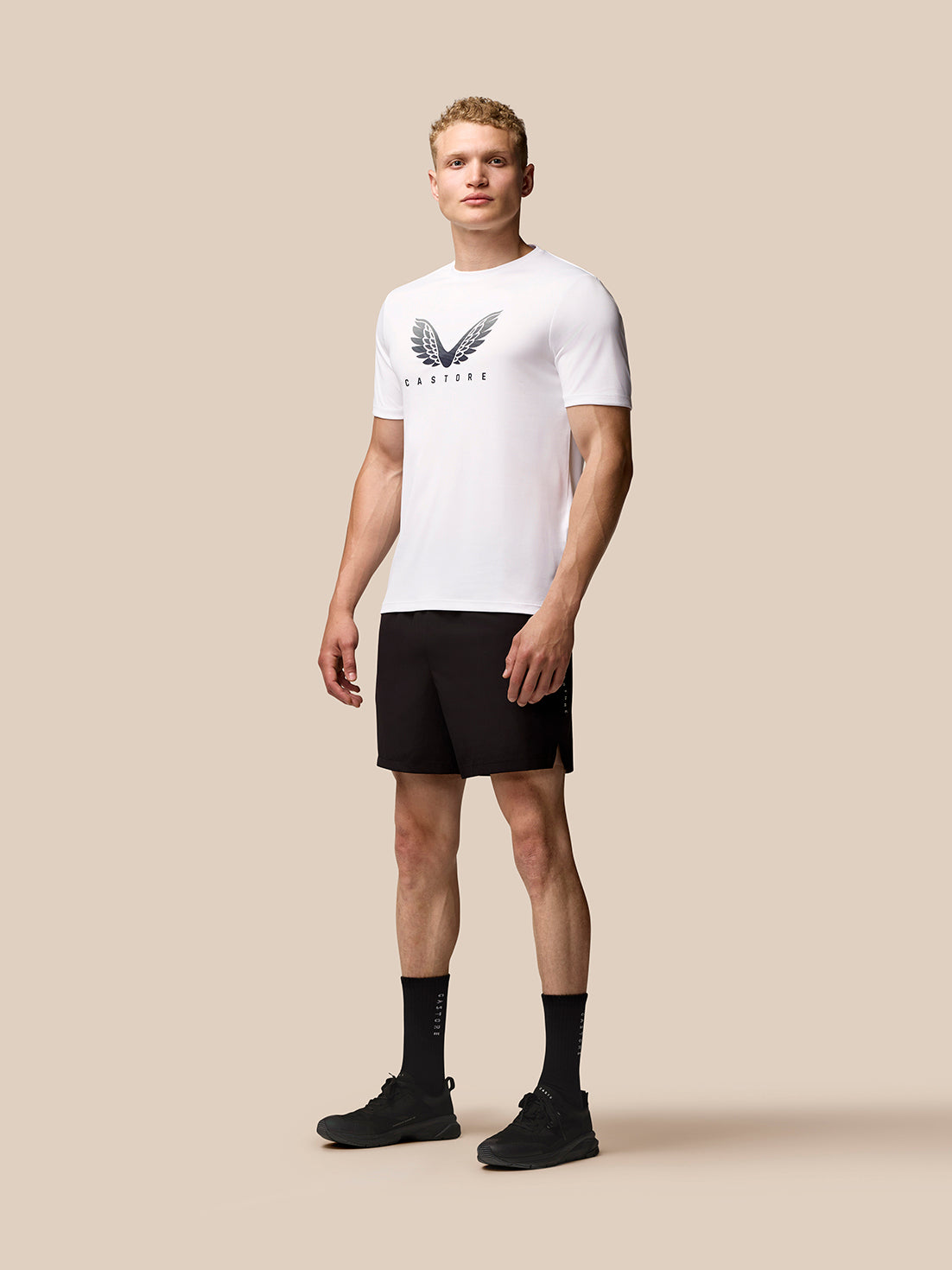 Male model wearing white Adapt Short Sleeve Graphic T Shirt with Castore wings logo and black shorts