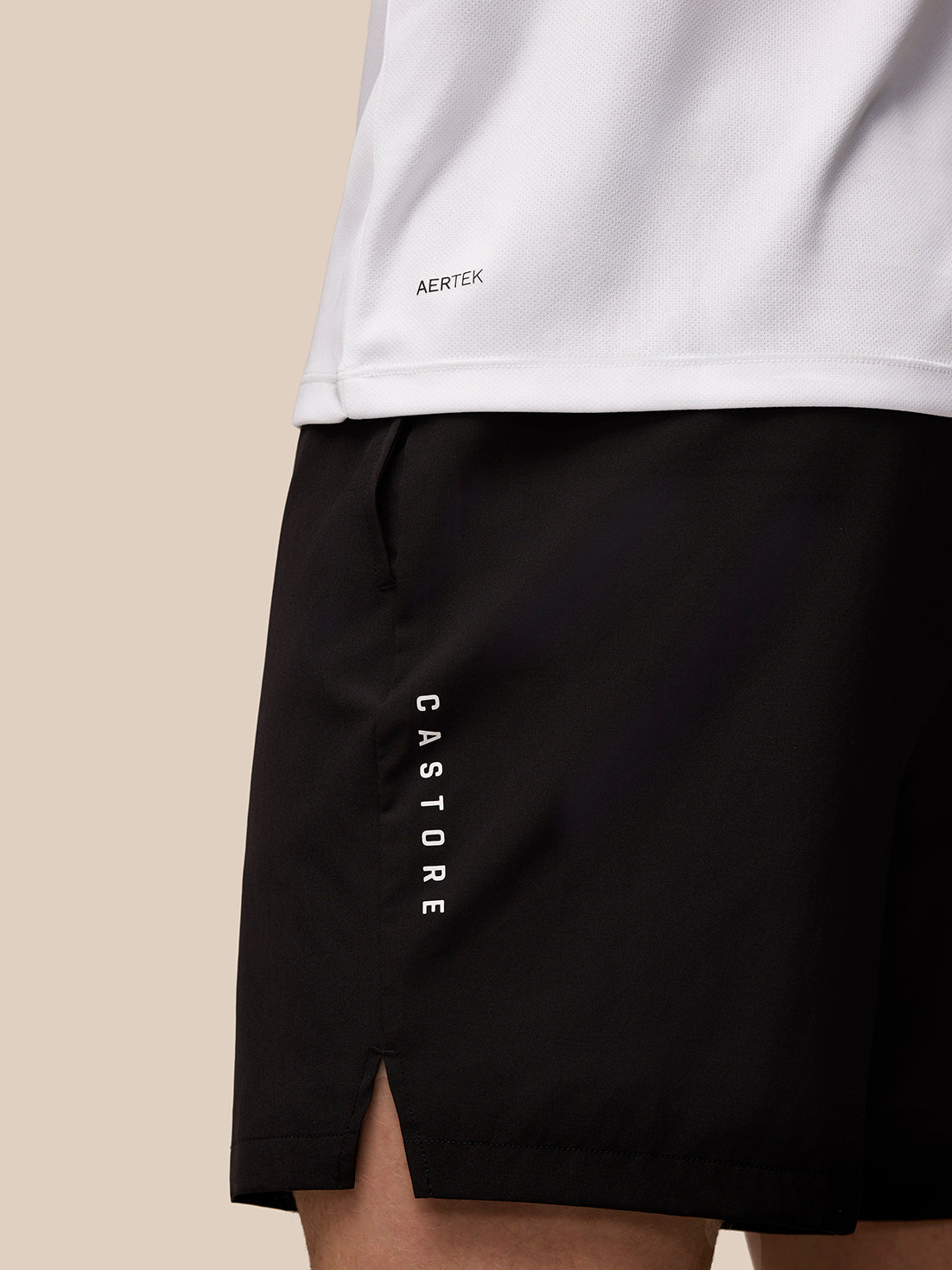 Close up of white Adapt Short Sleeve Graphic T Shirt hem with Aertek branding and black shorts with vertical Castore lettering