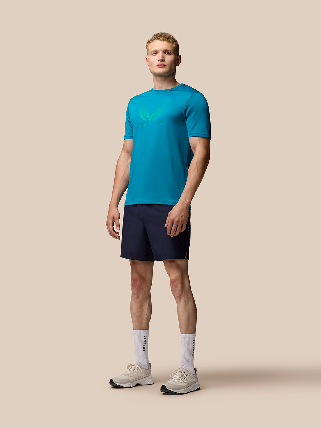 Full body shot of a male model wearing turquoise Adapt Short Sleeve Graphic T-Shirt with navy shorts