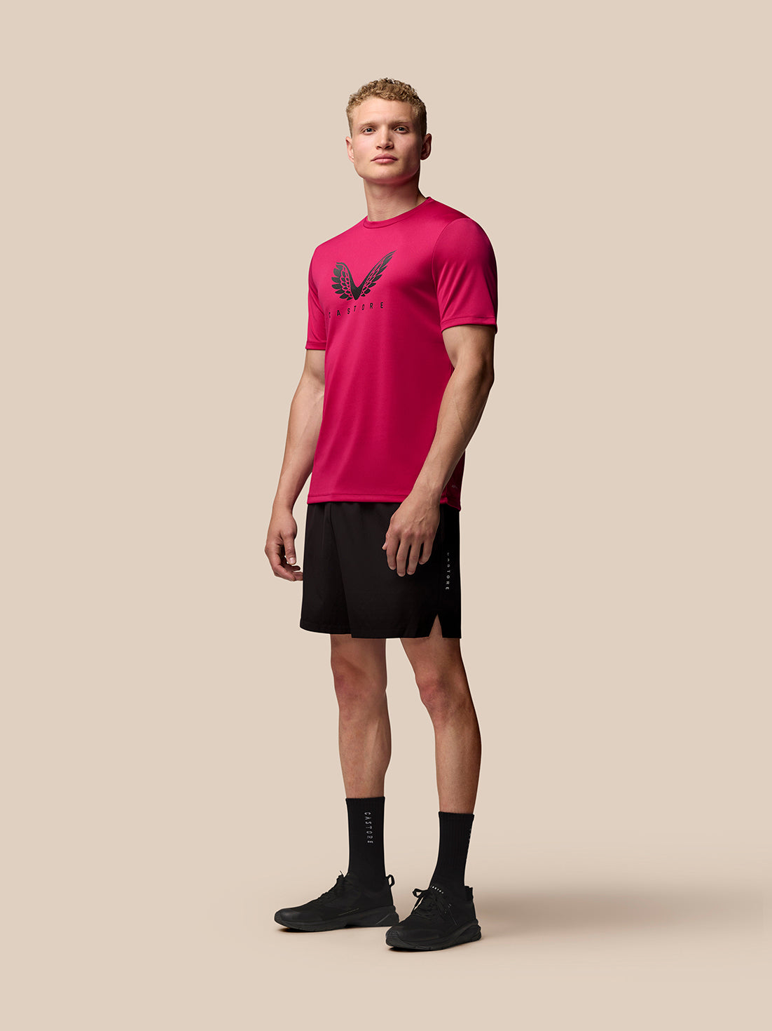 Full body side view of male model in pink Adapt Training T-Shirt with wings logo and black shorts.