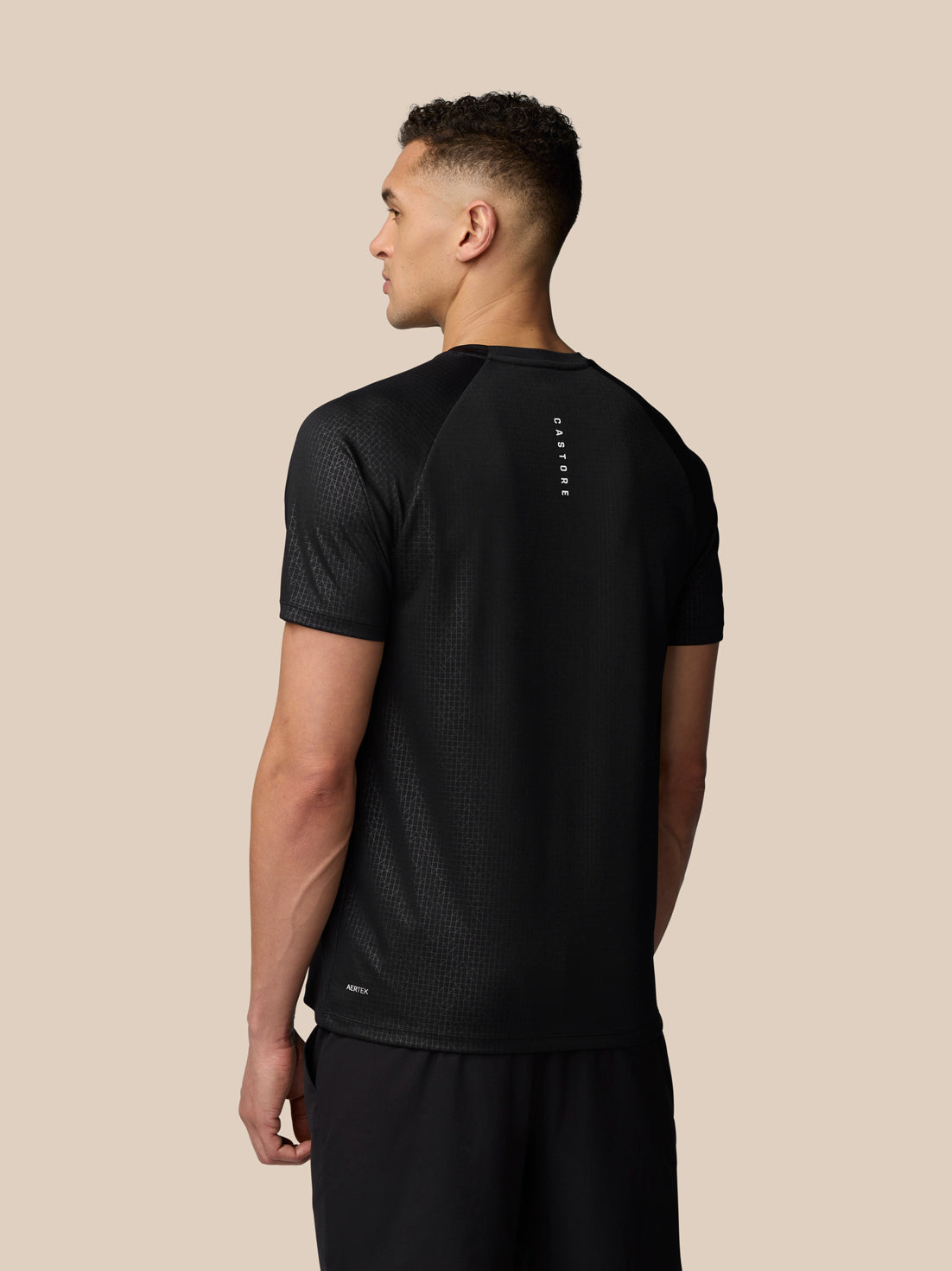 Back view of a male model wearing black Adapt Training T Shirt with a vertical Castore logo on the upper back.