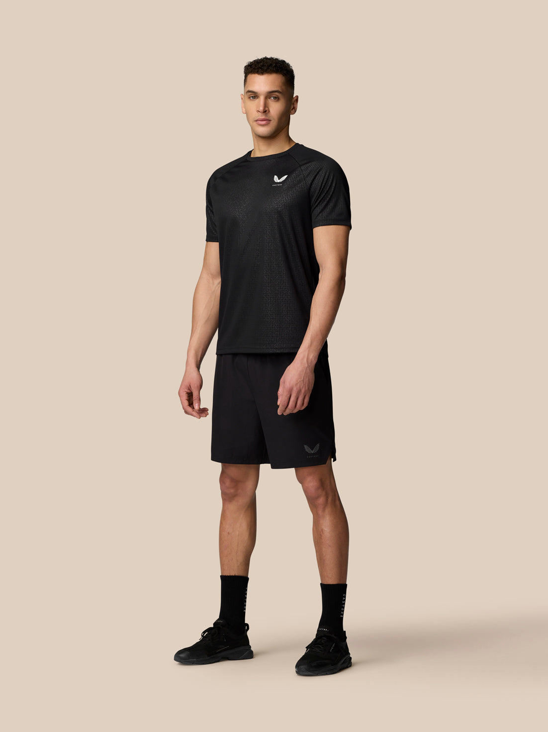 Three quarter view of a man in black Adapt Training T Shirt with all over print and branding on the chest.