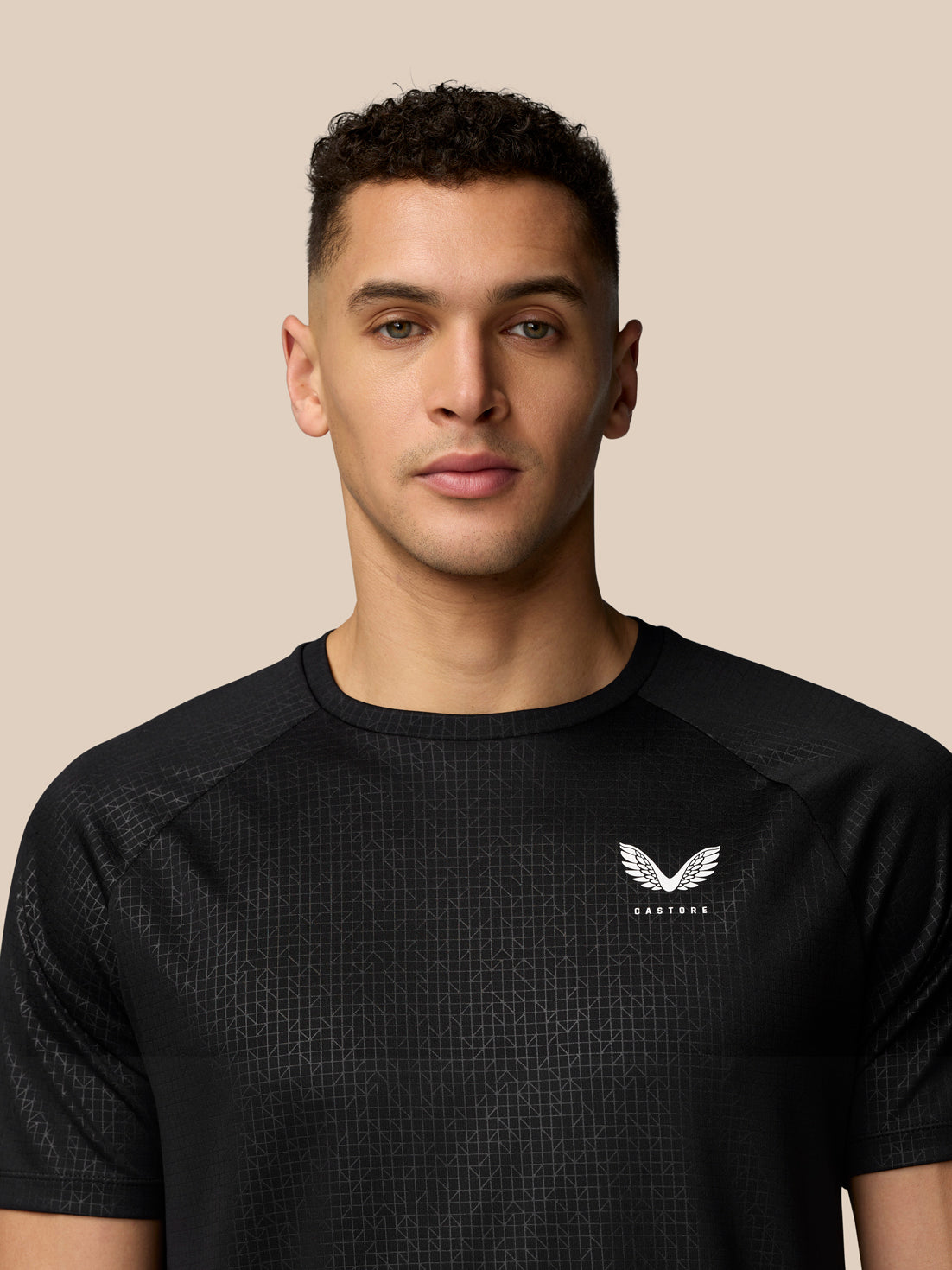 Male model wearing black Adapt Training T-Shirt with Castore logo on chest and all over geometric print.
