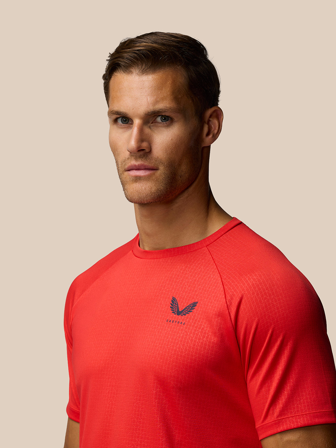 Side view of male model in red Adapt Training T-Shirt showing chest Castore logo and grid texture