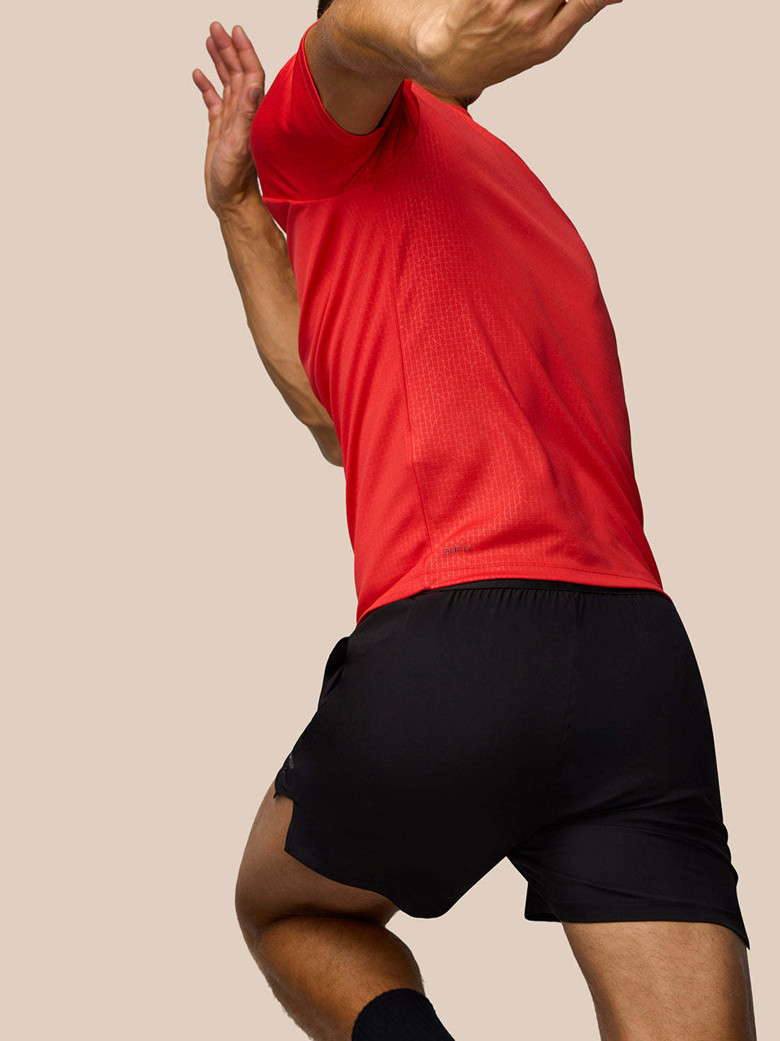 Back view of male model in red Adapt Training T-Shirt with Aertek label at hem and faint grid pattern