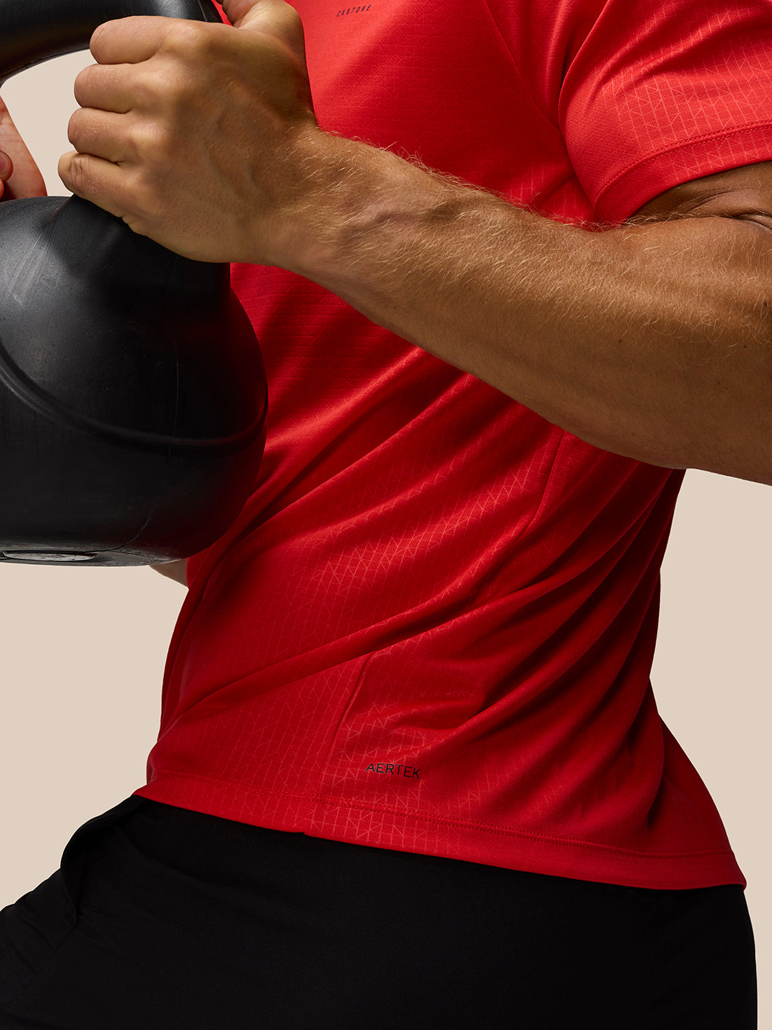 Close-up of a person in a red Adapt Training T Shirt gripping a kettlebell, showcasing raglan sleeves and all over print.