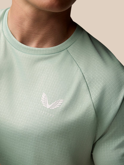 Close-up of mint green Adapt Training T Shirt showing a textured geometric pattern and Castore logo on the chest