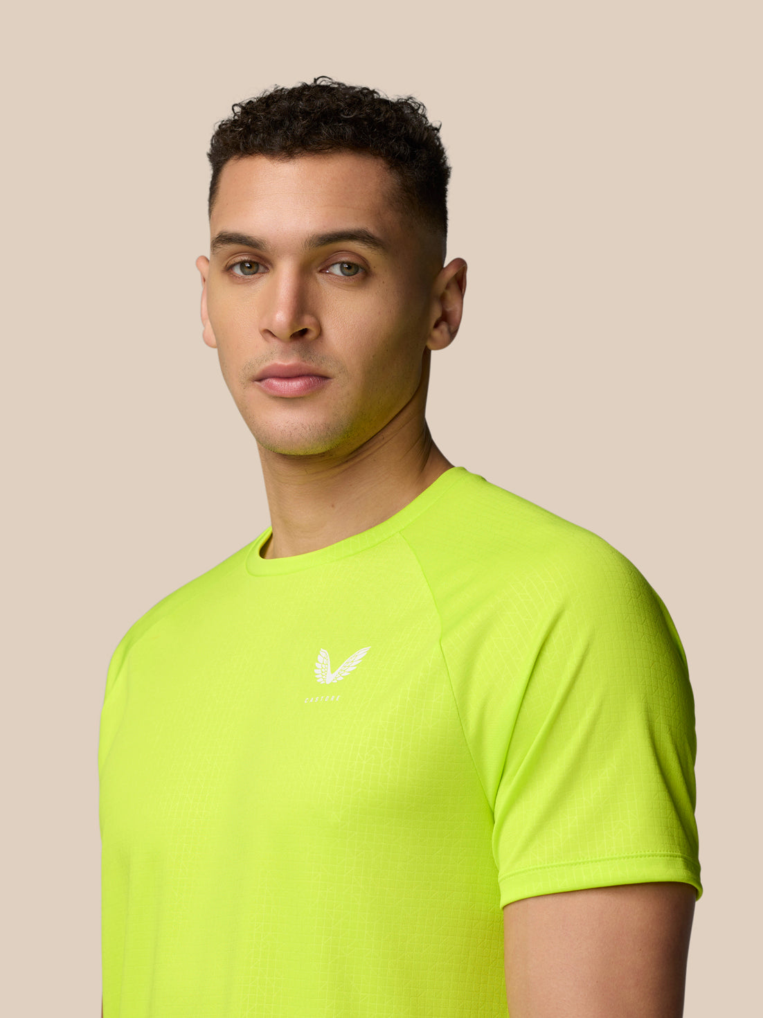 Male model wearing neon lime Adapt Training T-Shirt with Castore logo on chest against a beige background.