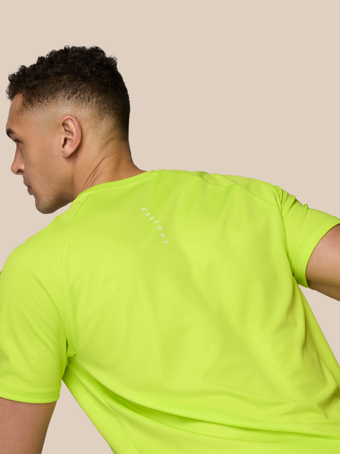 Rear view of male model in neon lime Adapt Training T-Shirt showing Castore branding along the upper back.