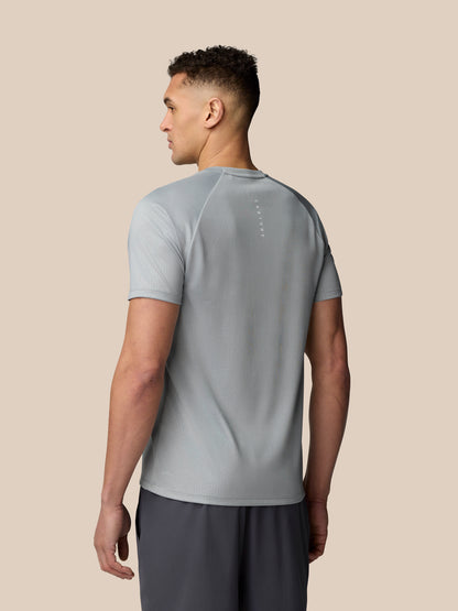 Back view of a man in light grey Adapt Training T Shirt with vertical Castore branding on the upper back and faint shoulder pattern