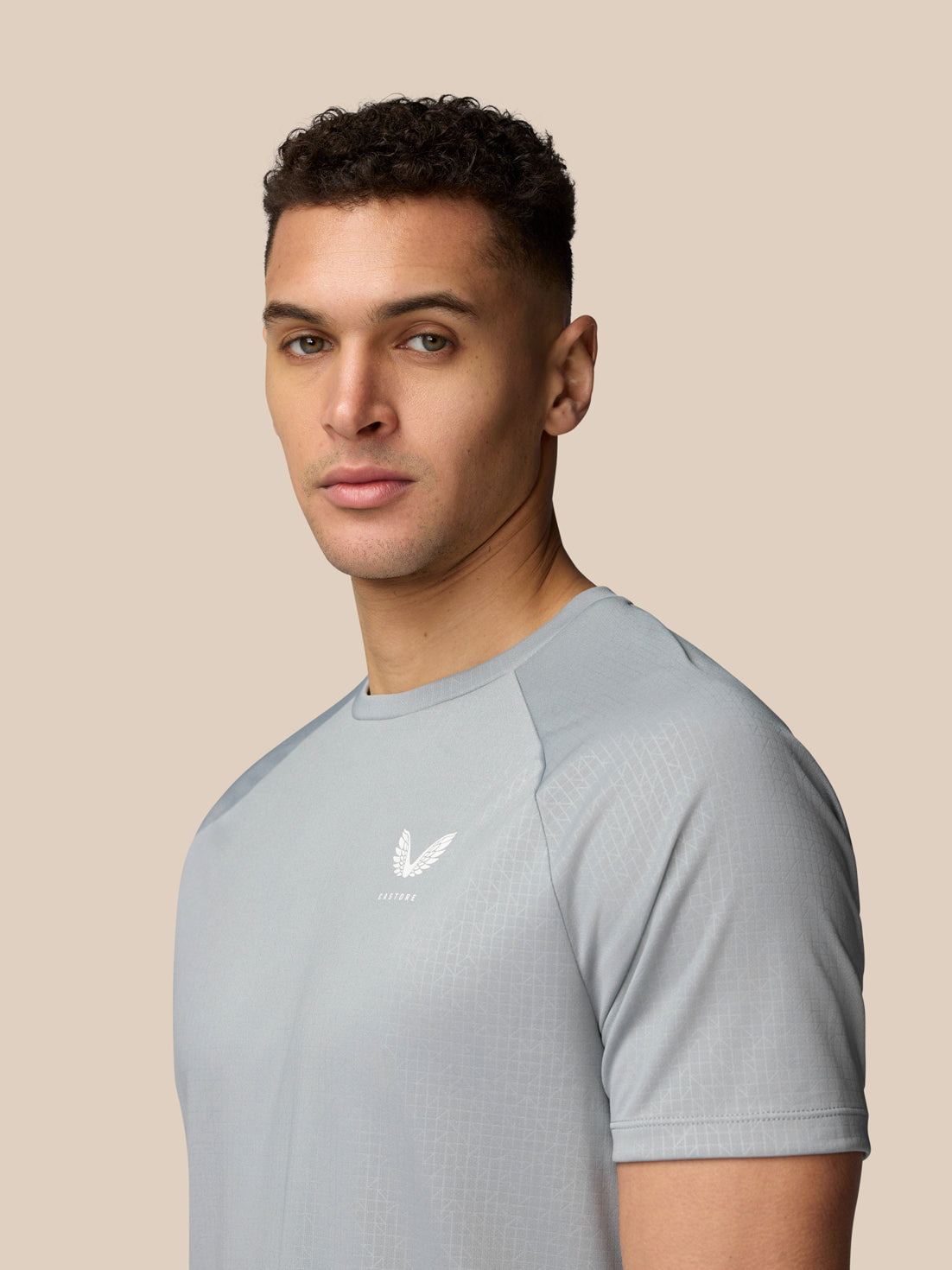 Three quarter view of a man wearing light grey Adapt Training T Shirt showing Castore logo on the chest and pale grid pattern across the fabric