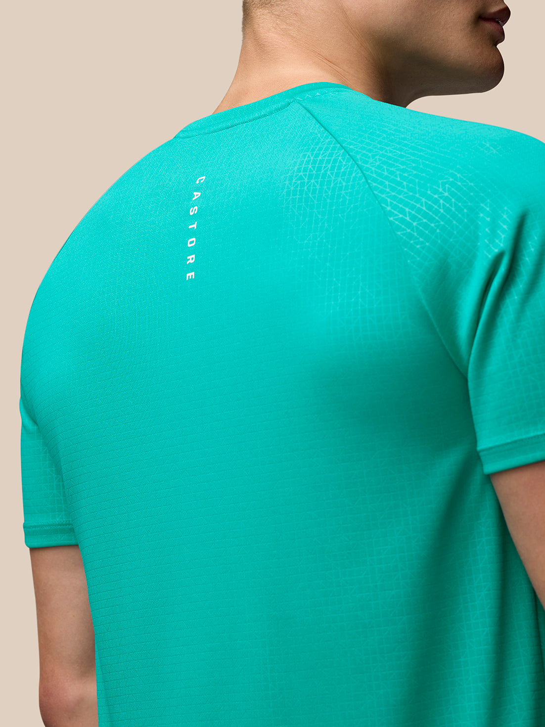 Back close up in bright aqua Adapt Training T shirt showing vertical Castore branding along the back and subtle geometric texture