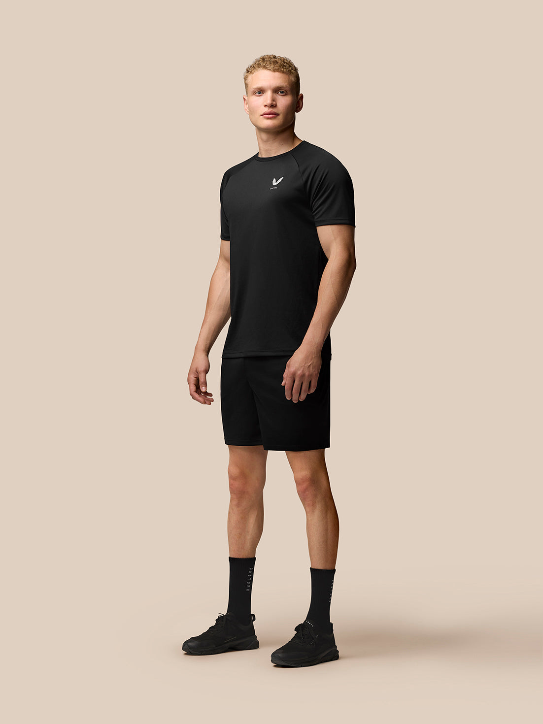 Full body shot of male model in black Adapt Short Sleeve T Shirt with Castore logo on chest and black shorts