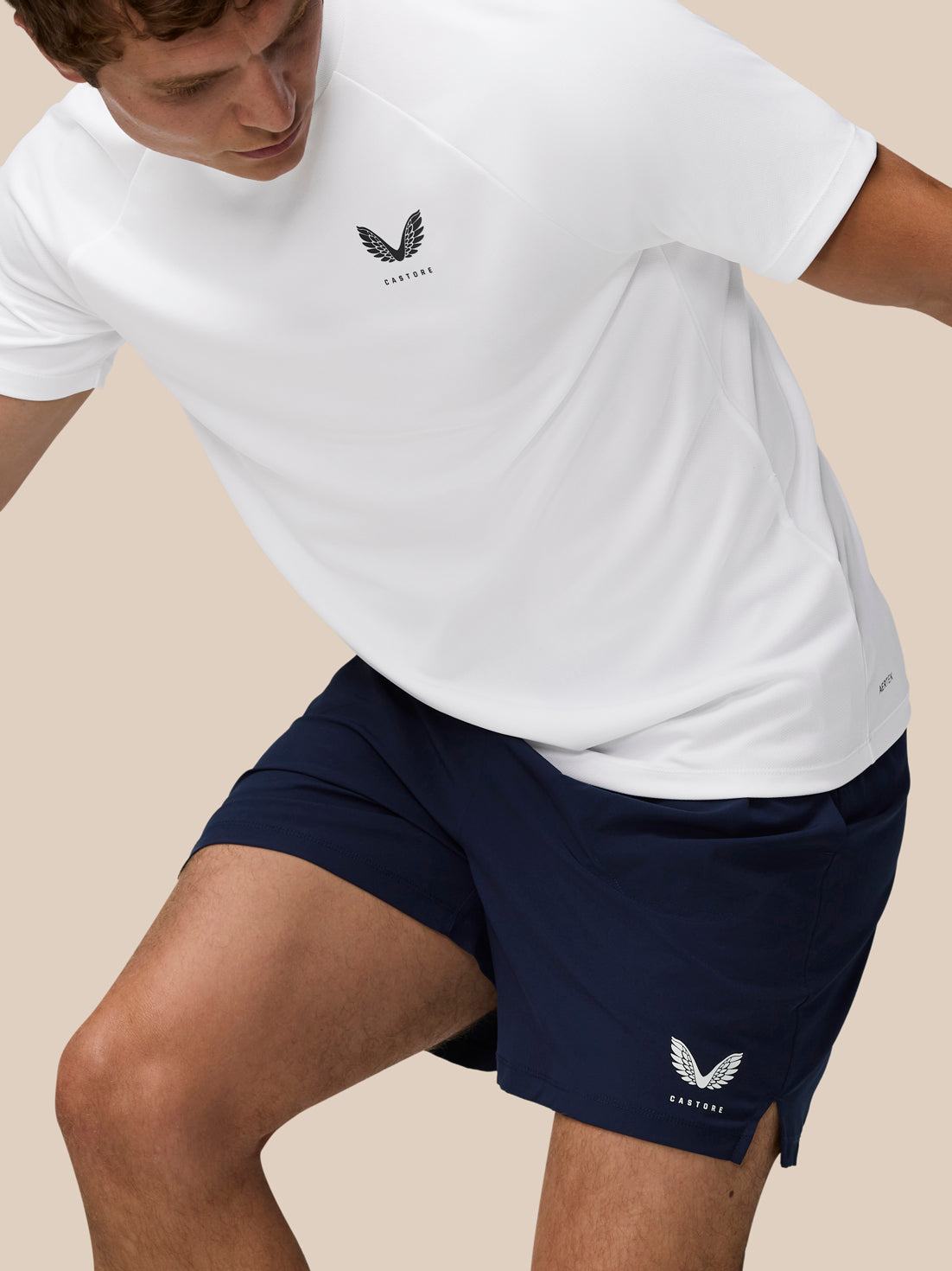 Athlete wearing white Adapt Training T-Shirt and navy shorts in motion with Castore crest on the chest