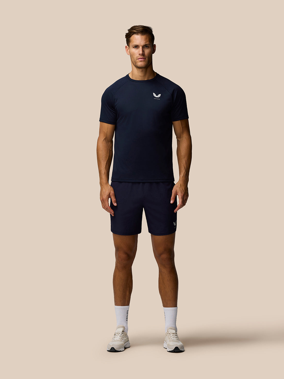 Front view of a male model wearing the midnight navy Adapt Training T-Shirt with Castore branding, paired with navy shorts.
