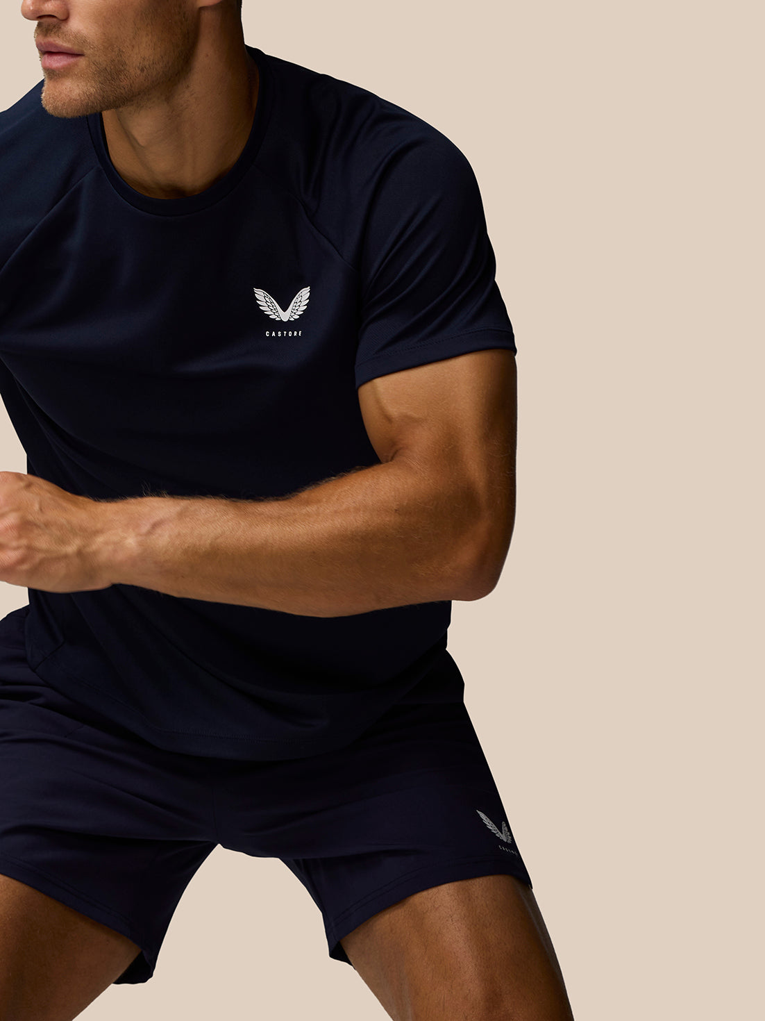 Side view of a male model wearing midnight navy Adapt Training T-Shirt showing a chest Castore logo and a small logo on the shorts.