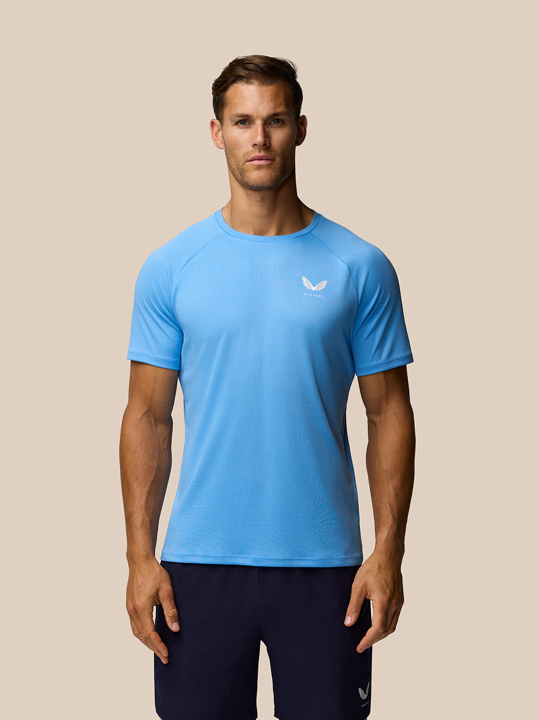 Male model in light blue Adapt Training T-Shirt with Castore logo on the left chest and navy shorts.