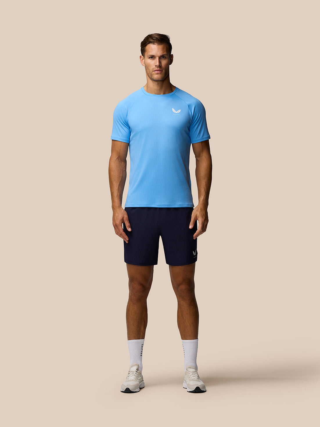 Full-body shot of male model in light blue Adapt Training T-Shirt and navy shorts with Castore logo on the chest and a small logo on the shorts.