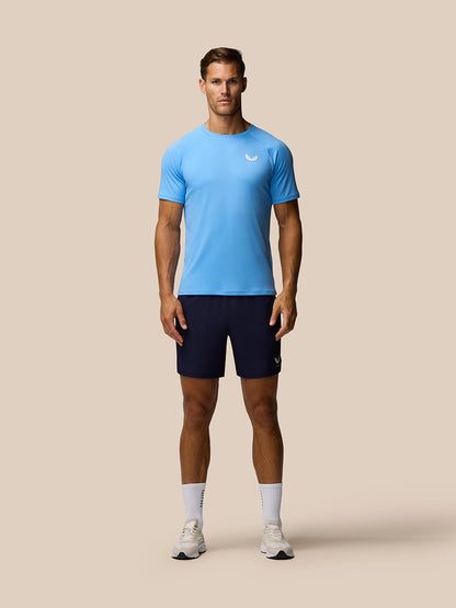 Full-body shot of male model in light blue Adapt Training T-Shirt and navy shorts with Castore logo on the chest and a small logo on the shorts.