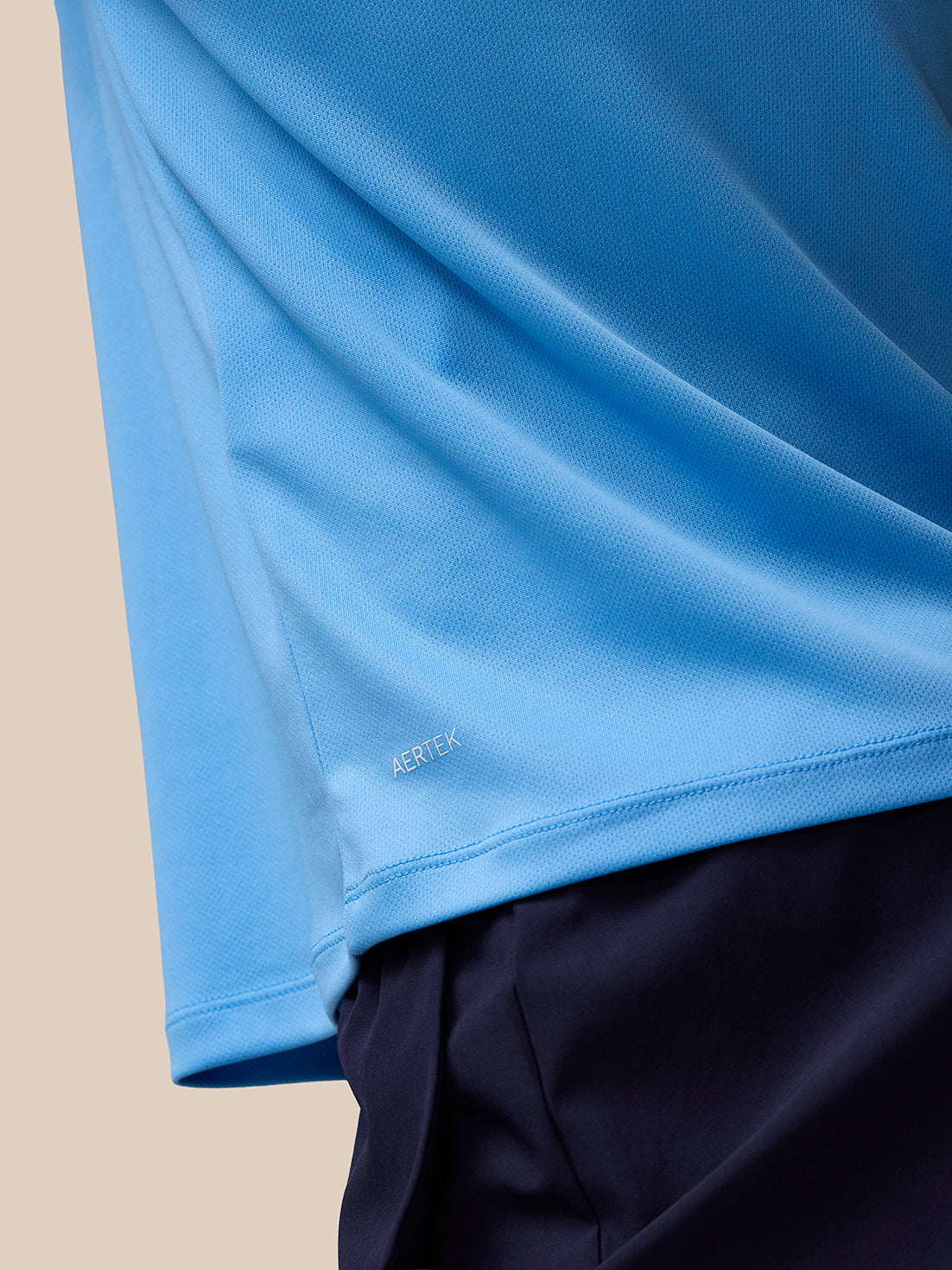 Close up of light blue fabric with AerTek branding near the hem of the Adapt Training T Shirt