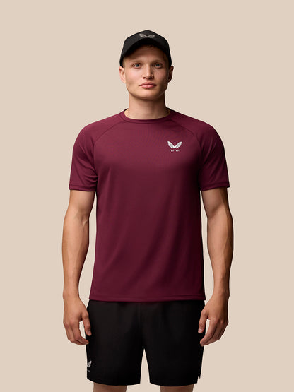 Model wearing burgundy Adapt Training T-Shirt with small white chest logo and a black cap