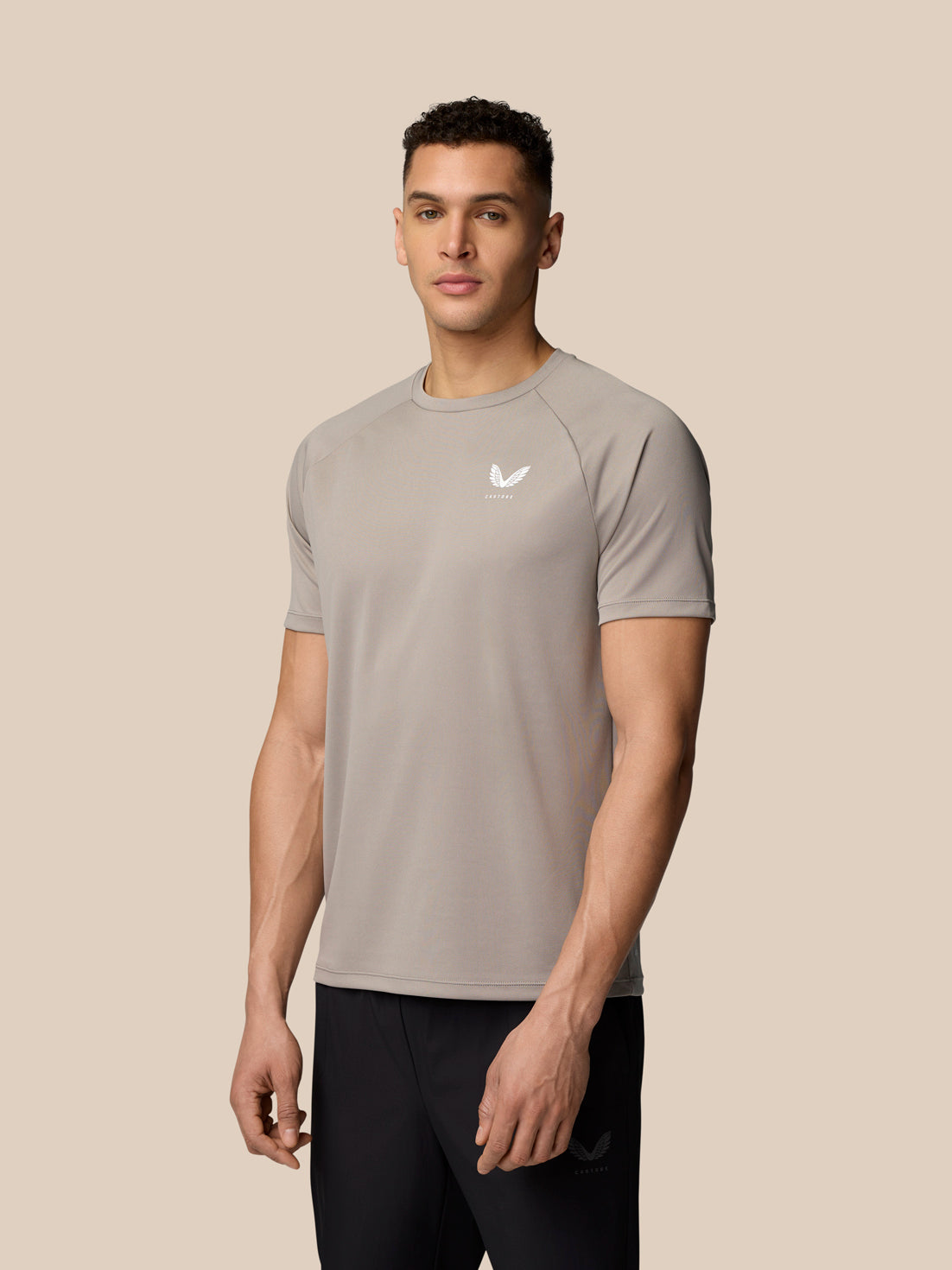 Male model wearing taupe Adapt Training T-Shirt with Castore logo on the chest against a beige backdrop