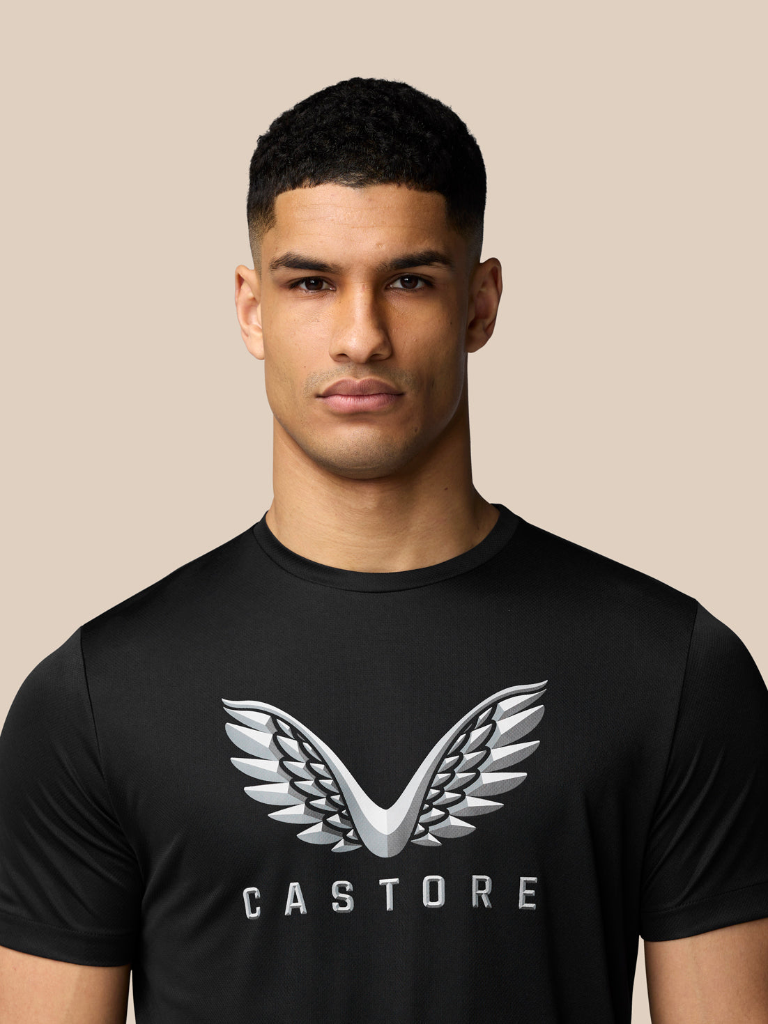 Close up of a man wearing a black graphic training T shirt with a large Castore wings logo on the chest