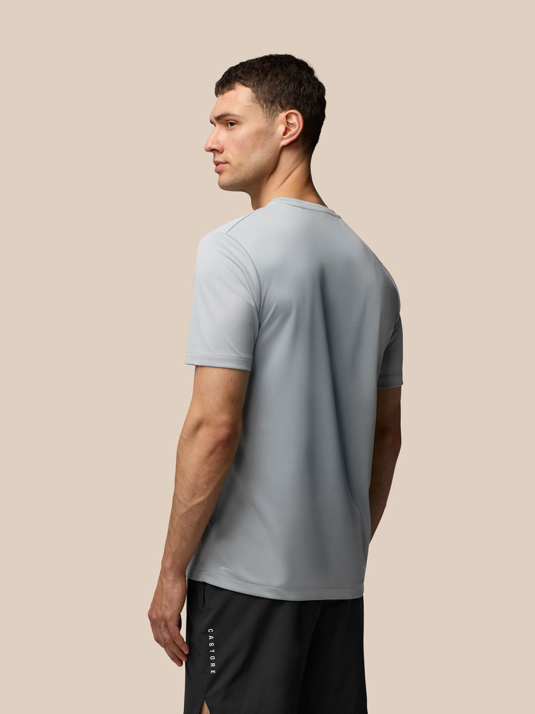 Male model wearing grey Adapt Graphic Training T-Shirt shown from the side with the wing chest graphic.