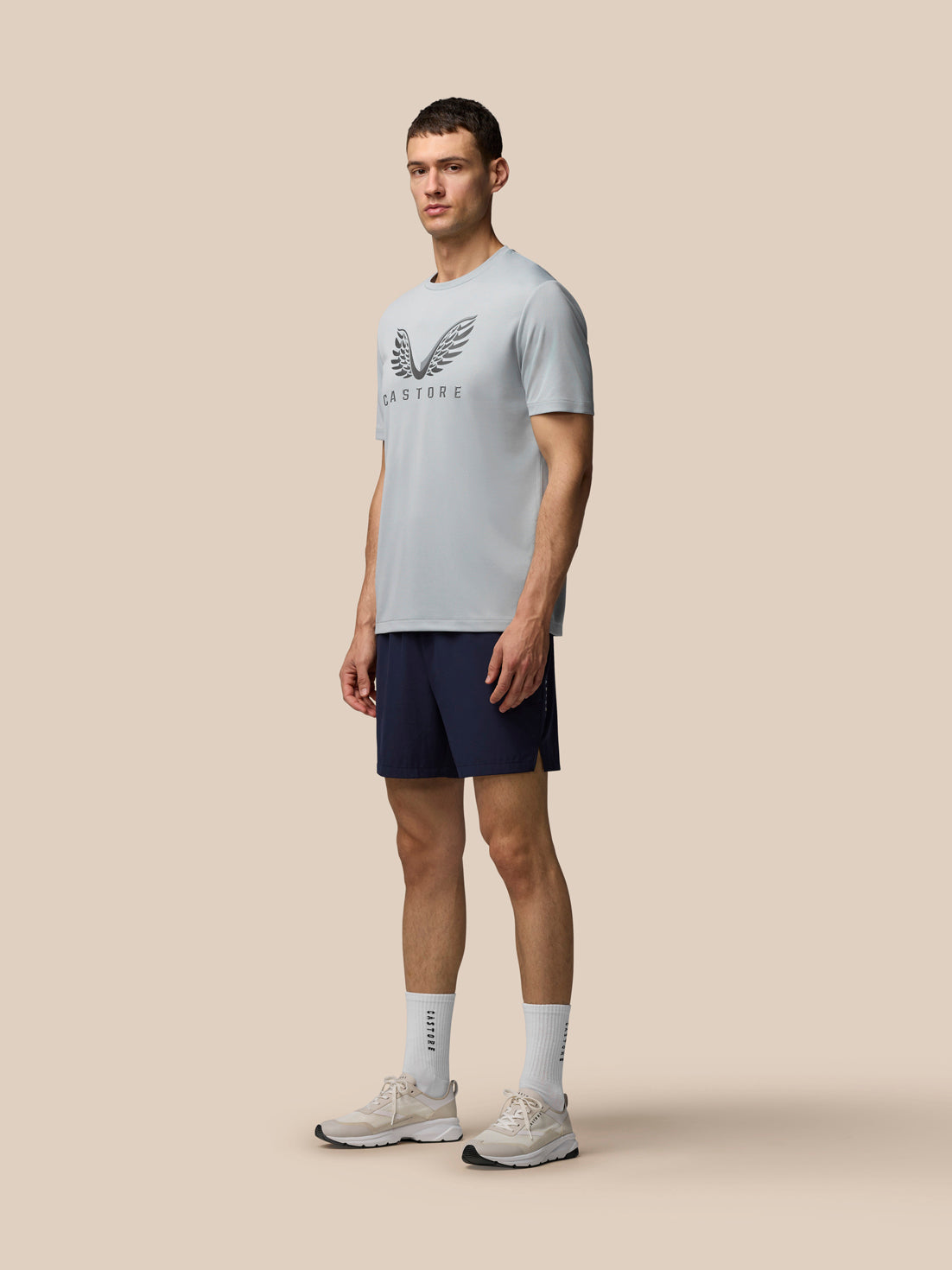 Full body side view of male model wearing grey Adapt Graphic Training T-Shirt with navy shorts