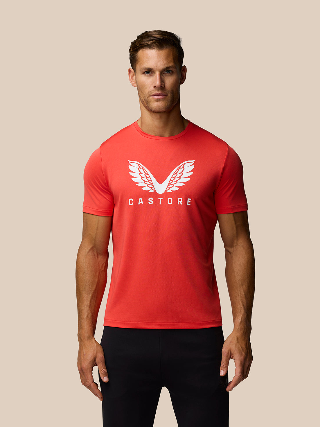 Male model wearing a poppy red graphic training T shirt with white wing logo and CASTORE branding