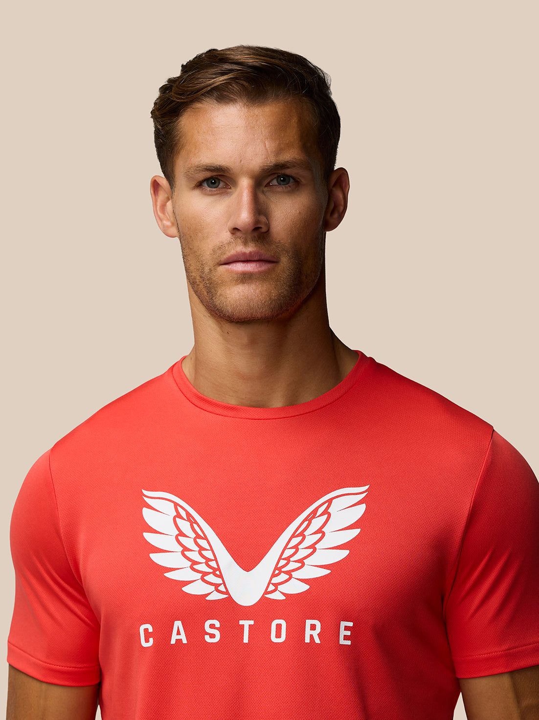 Male model wearing red graphic training T shirt with white wing logo and Castore branding