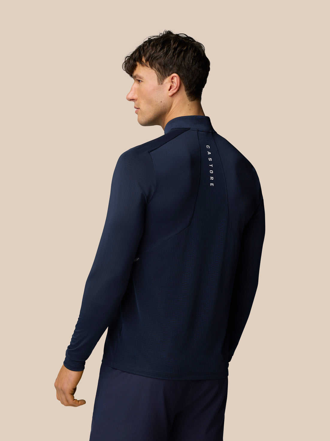 Back view of male model in navy Apex Training 1/4 Zip Top with vertical Castore branding along the back