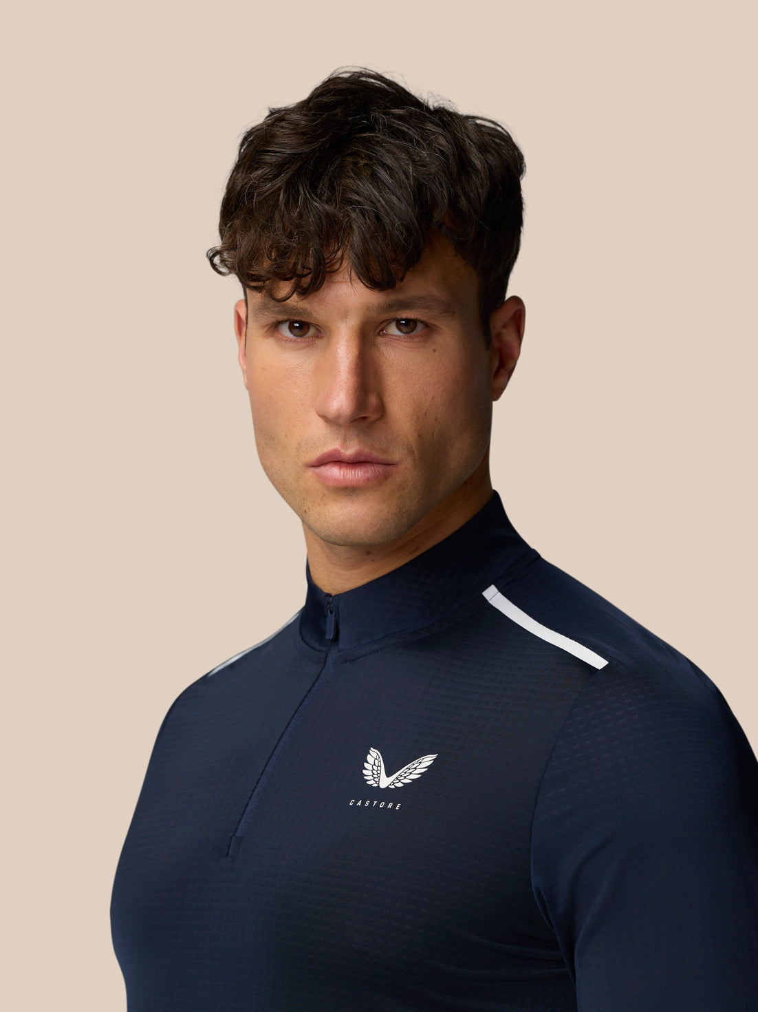 Three quarter profile of male model in navy Apex Training top with white shoulder stripe and Castore logo on chest