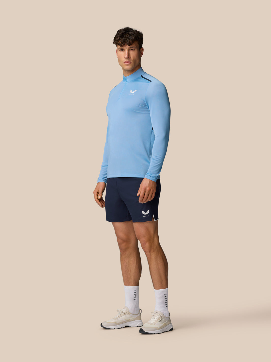 Male model wearing sky blue Apex Training long sleeve quarter zip top with logo on chest and navy shorts