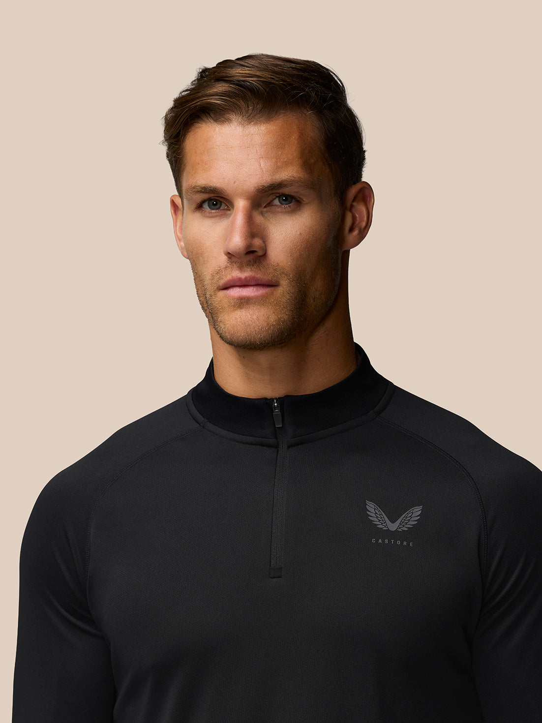Close-up of male model wearing black Adapt Training top with front quarter zip and left chest logo.