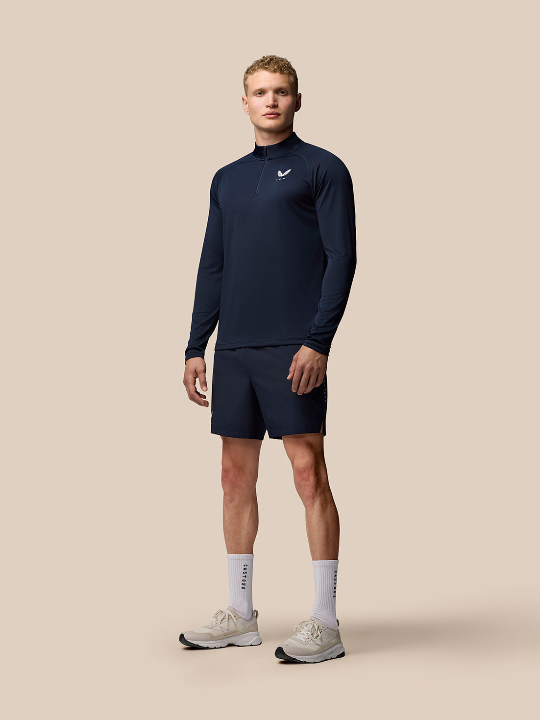 Man wearing navy Adapt Training 1/4 Zip Top with stand collar and raglan sleeves, paired with navy shorts