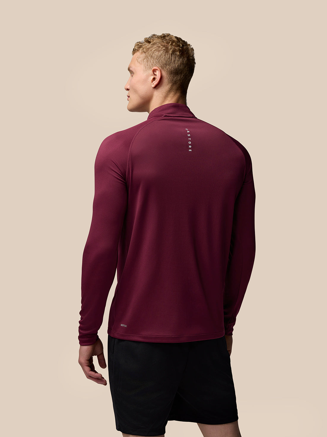 Back view of a model in burgundy Adapt Training long sleeve quarter zip top highlighting a vertical logo on the upper back