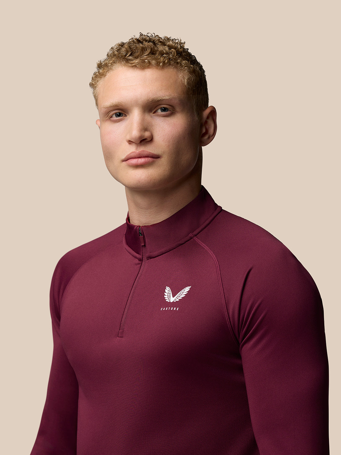 Portrait of a model wearing burgundy Adapt Training top with Castore crest on the left chest
