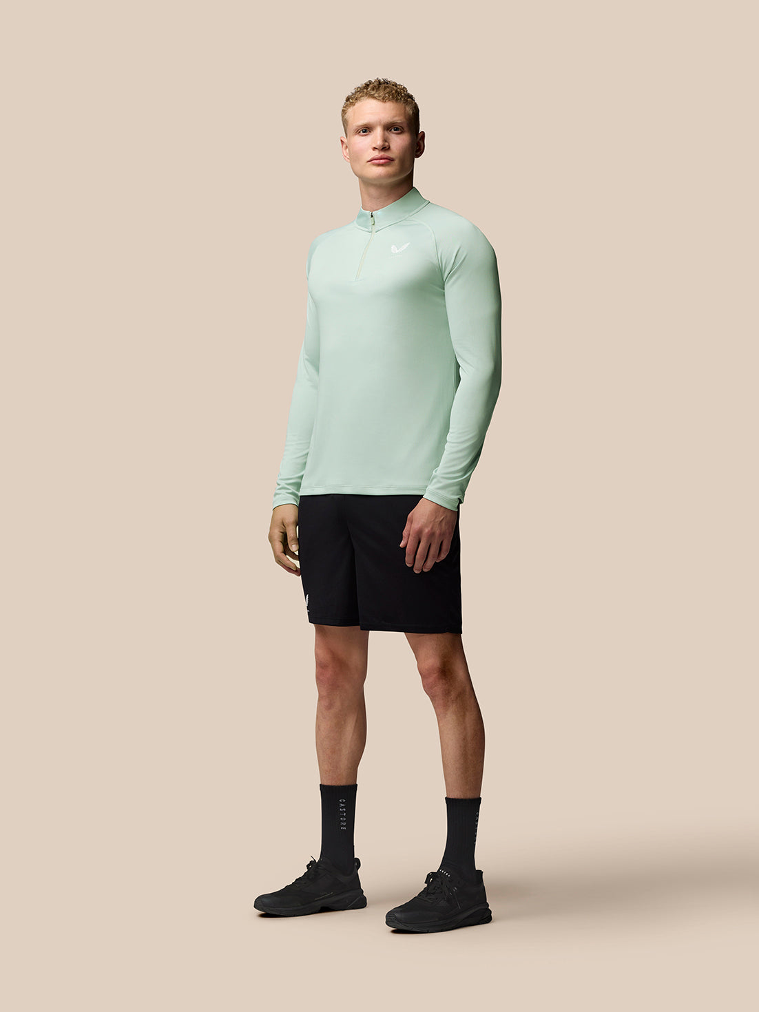 Male model wearing mint green Adapt Training long sleeve quarter zip top with stand collar and Castore branding on the chest.