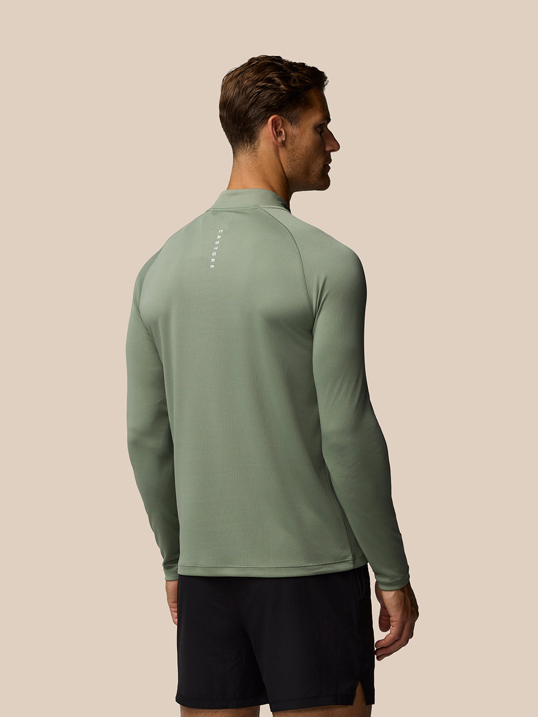 Back view of a man wearing Adapt Training 1/4 Zip Top in Thyme Mint, showcasing raglan shoulders and the vertical Castore logo.