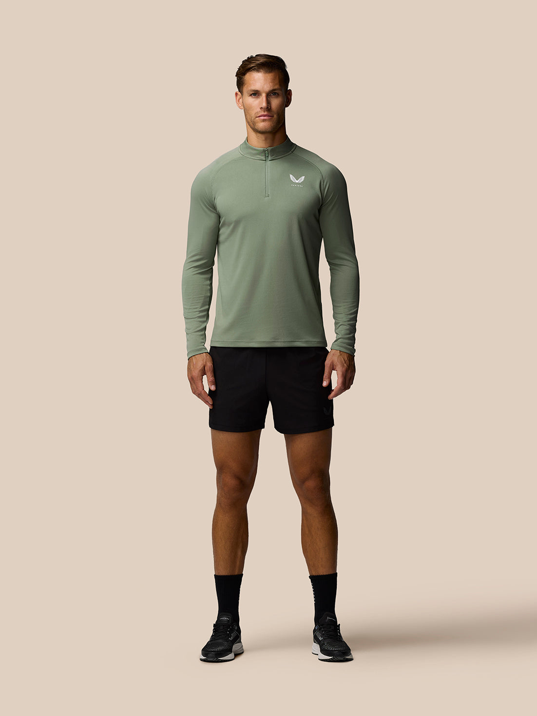 Male model wearing thyme green Adapt Training 1/4 Zip Top with white left chest logo and black shorts.