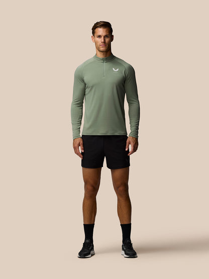 Male model wearing thyme green Adapt Training 1/4 Zip Top with white left chest logo and black shorts.