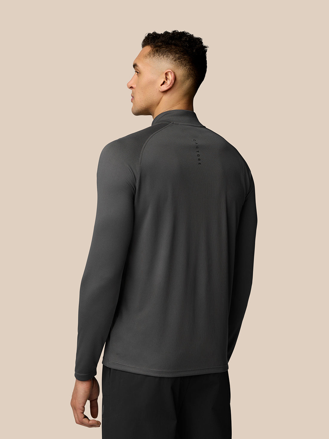 Back view of a model wearing gunmetal Adapt Training 1/4 Zip Top with raglan sleeves and Castore branding along the upper back